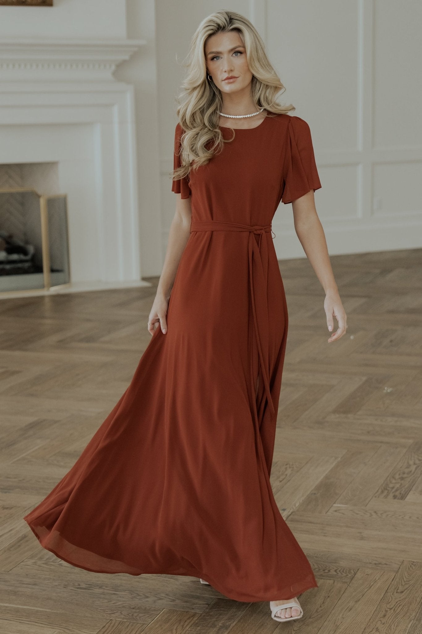 Model wearing Naomi cinnamon chiffon maxi dress walking to show movement, drape, and left leg slit in motion.