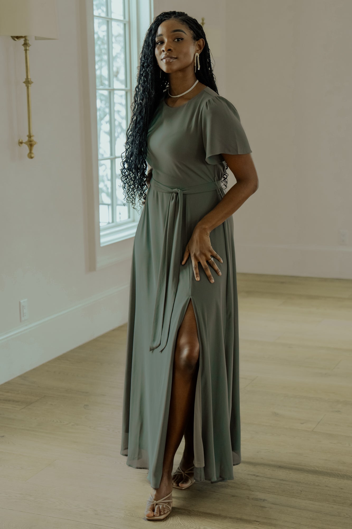 Full-length side view of Naomi chiffon maxi dress in dark sage highlighting short flutter sleeves, left-leg slit, and flowing skirt movement.