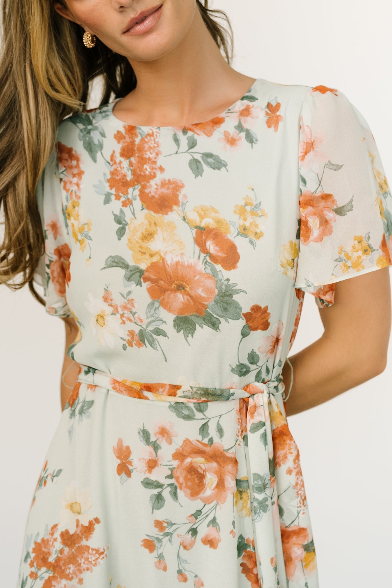 Detail of short flutter sleeve and sheer chiffon overlay with warm rust and yellow floral pattern on a light-sage background.