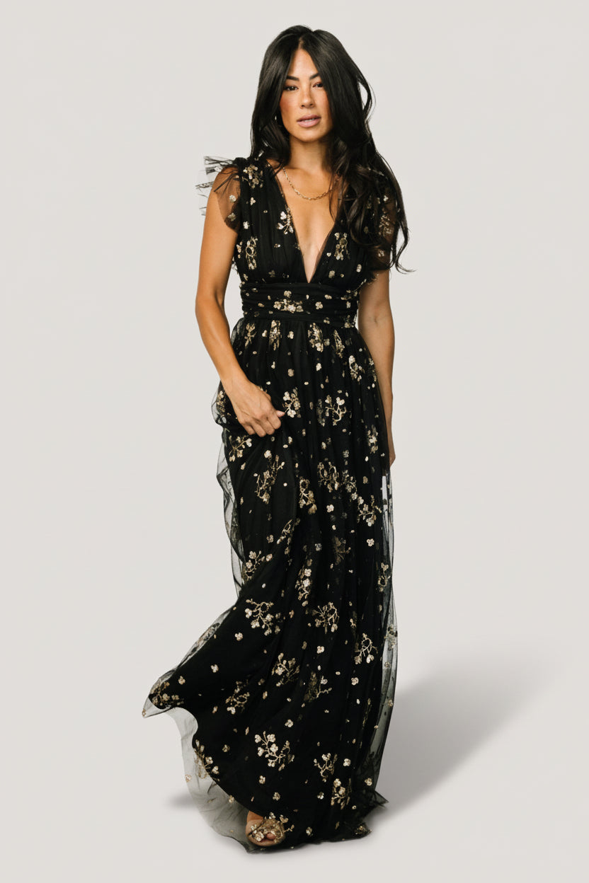 Front view of Natalia black-and-gold maxi dress showing deep V-front, high banded waist, and full-length skirt with glittery floral embellishments (model pose).