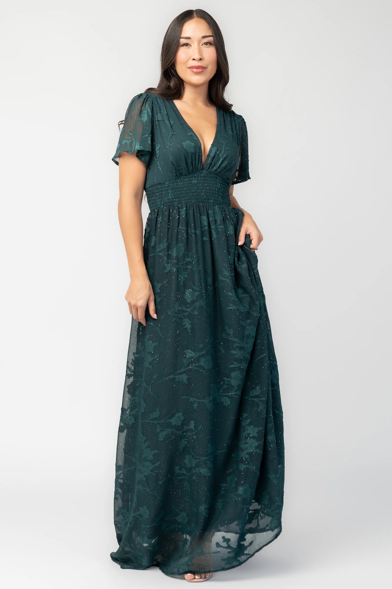 Noelle Maxi Dress in Dark Green Floral with silver sparkle, deep V-neck, flutter sleeves, smocked waist, and flowy skirt.