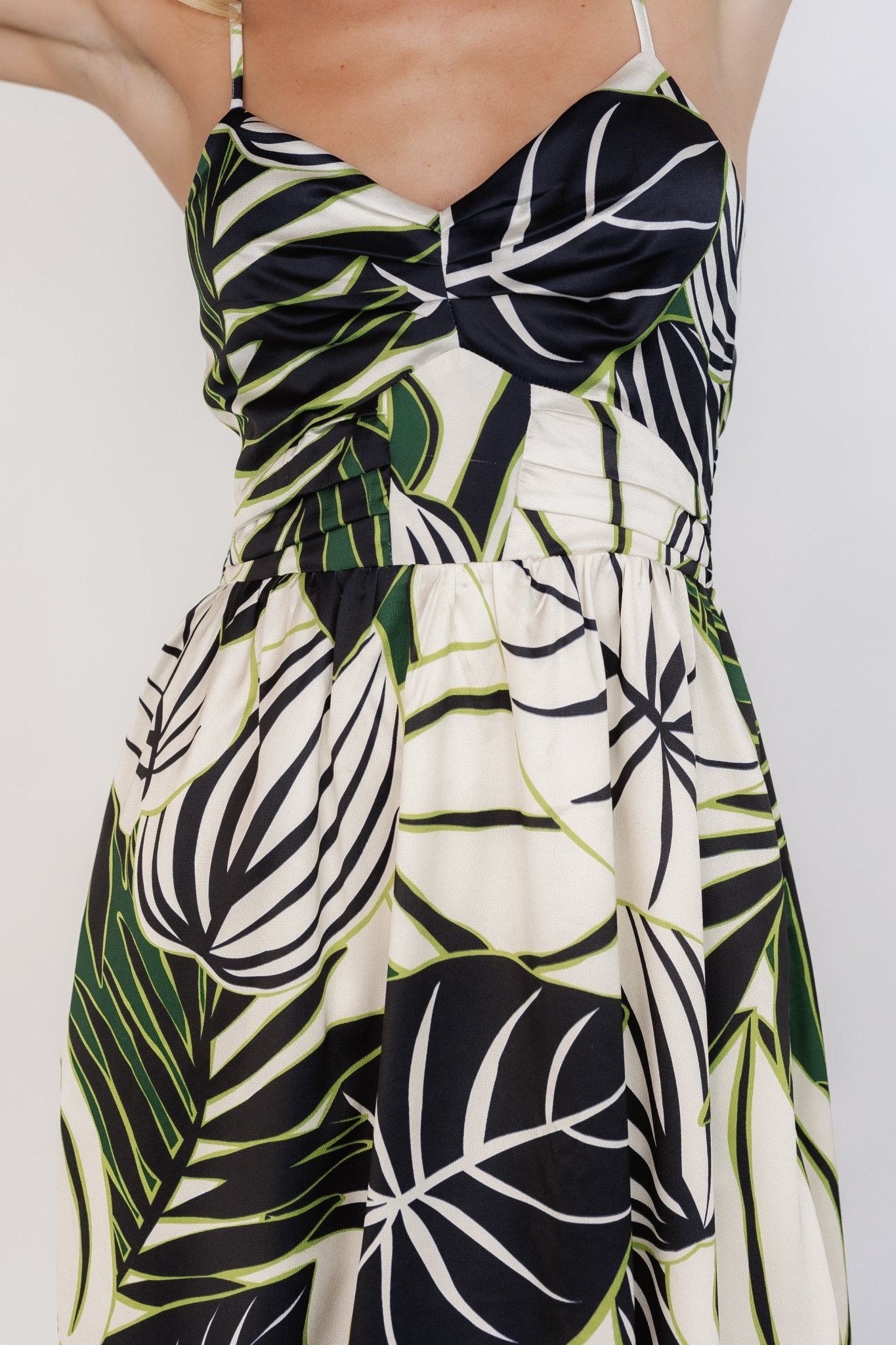 Close-up of bodice showing pleats, vertical center details and smooth satin-like texture of the black, green and ivory print.