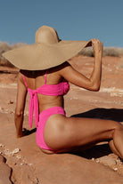 Side-angle of bright pink ribbed bikini bottom highlighting the banded waist, contoured seams, and moderate coverage in textured fabric.