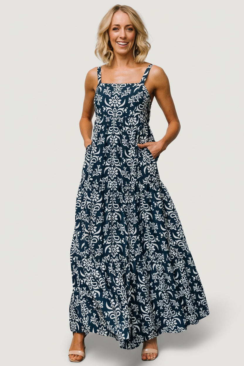 Front view of navy maxi dress with off-white print, square neckline, adjustable tank straps, paneled bodice and flowing tiered skirt for warm-weather wear.