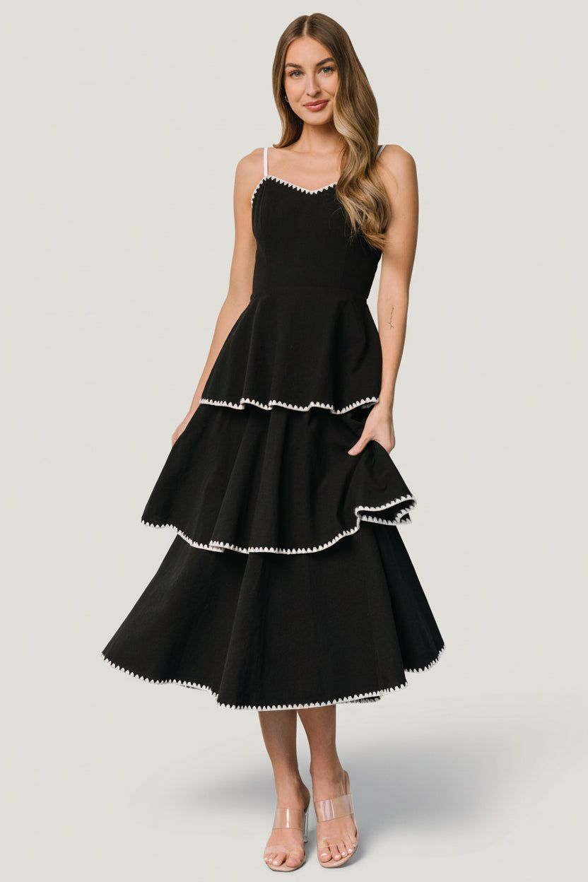 Front view of Odette Tiered midi dress in black with white embroidered triangle accents, V-neckline, and overlapping tiers.