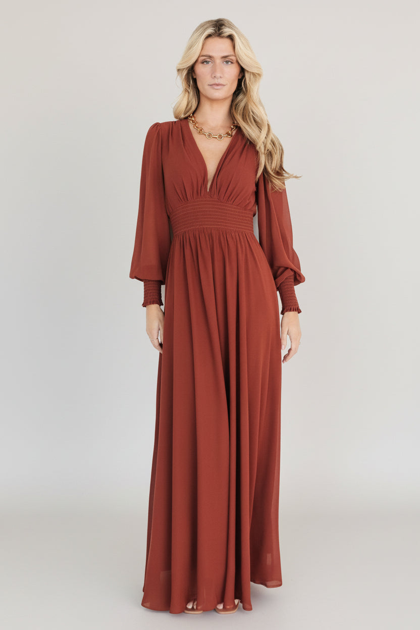 Three-quarter view of the Olivia Maxi Dress in cinnamon on a standing model, highlighting smocked waist, flowing skirt and flattering V-neck silhouette.