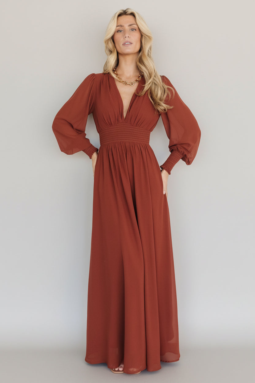 Front view of model wearing the Olivia Maxi Dress in cinnamon, showing long chiffon skirt, deep V-neck, smocked waist and long sleeves in full length.