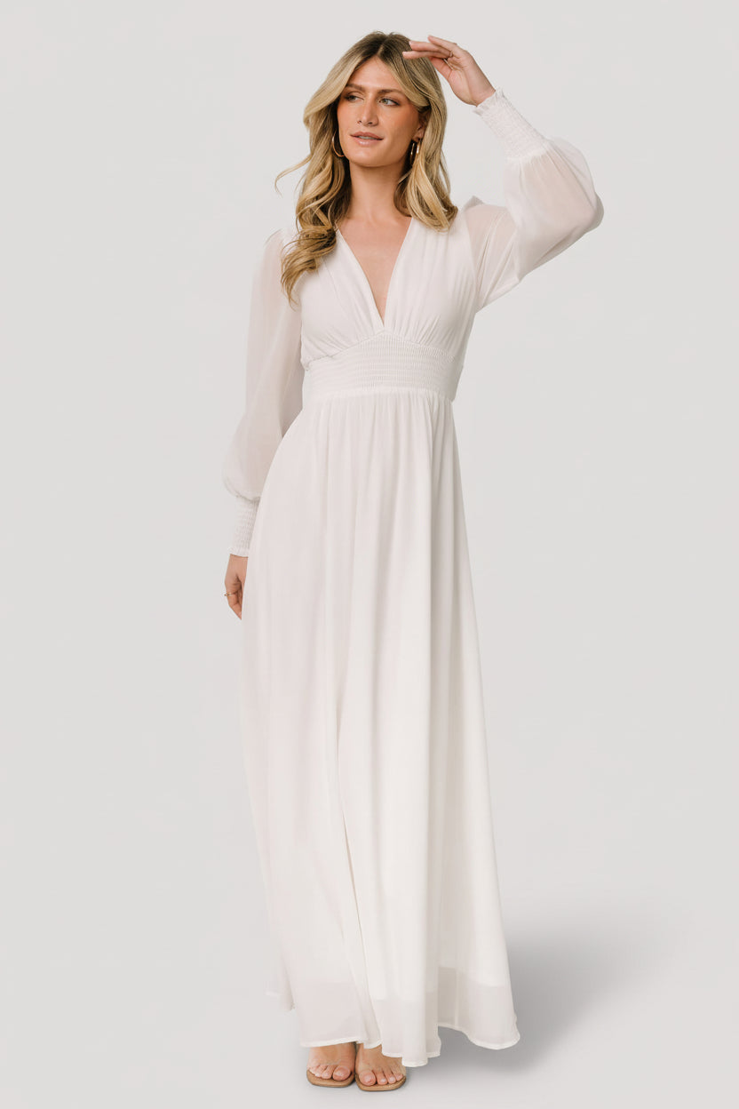 Front view of model wearing the Olivia Maxi Dress in white, flowing chiffon fabric, deep V-neckline, smocked waist and long smocked sleeves, full length.