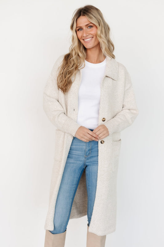 Side view of oatmeal longline cardigan styled over a top, highlighting drop sleeve with wide-ribbed cuff and relaxed longline silhouette.