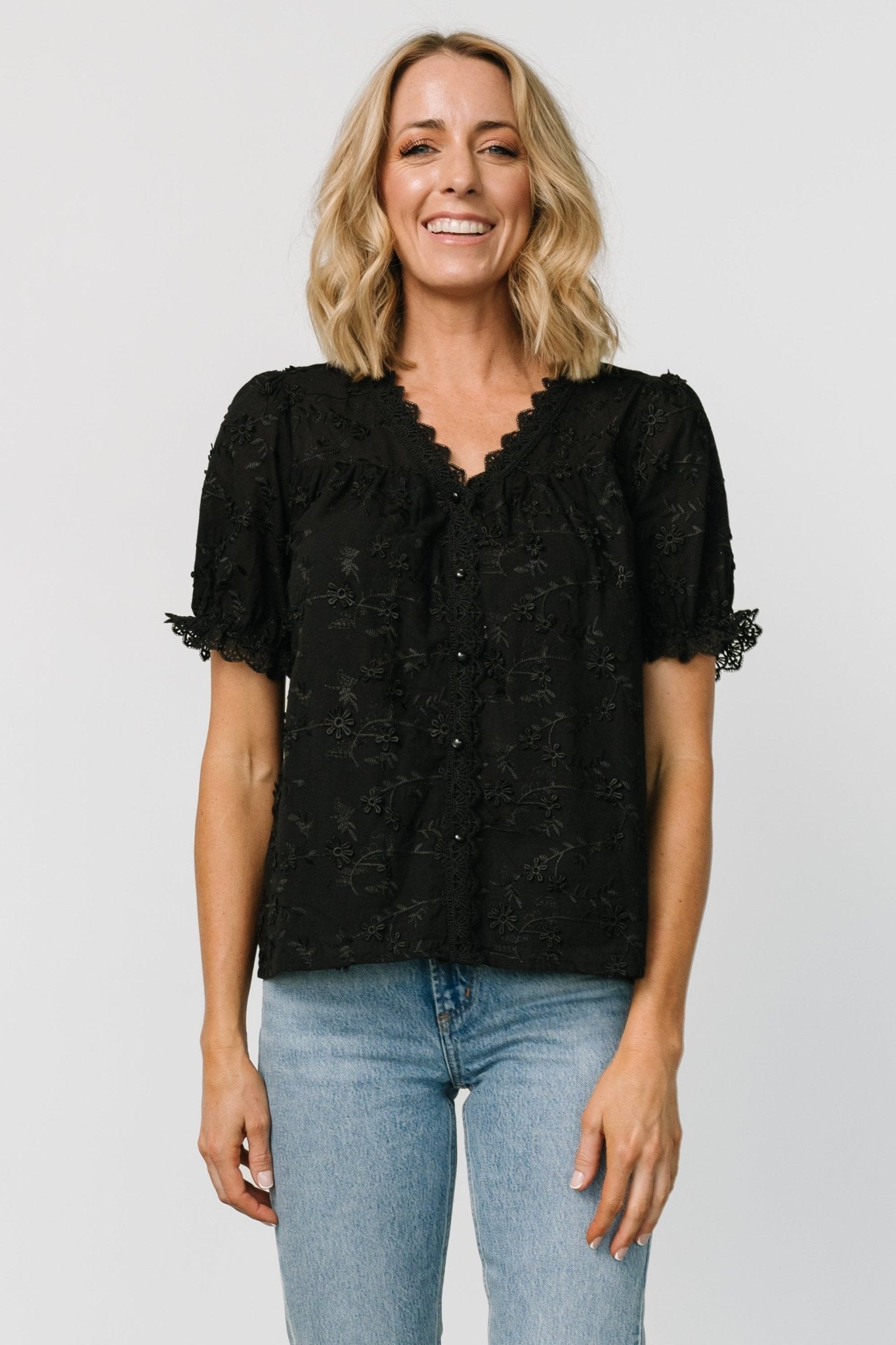 Front view of Pauline Embossed Top in black showing embroidered floral texture, lace V-neck, button placket, and relaxed swing silhouette.