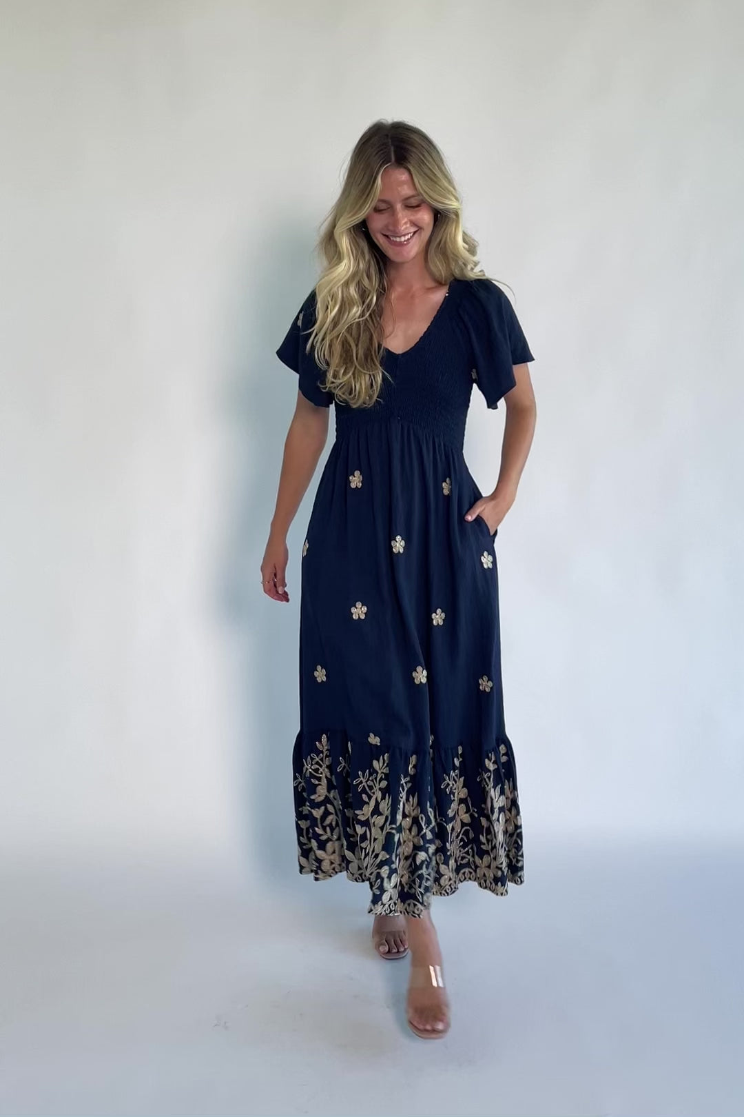 Model wearing a navy embroidered maxi dress with a V-neckline, flutter sleeves, and a smocked bodice.