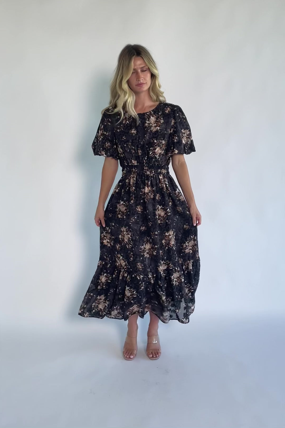 Model wearing a black floral midi dress with a round neckline, puff sleeves, and a smocked waist.
