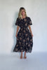 Model wearing a black floral midi dress with a round neckline, puff sleeves, and a smocked waist.