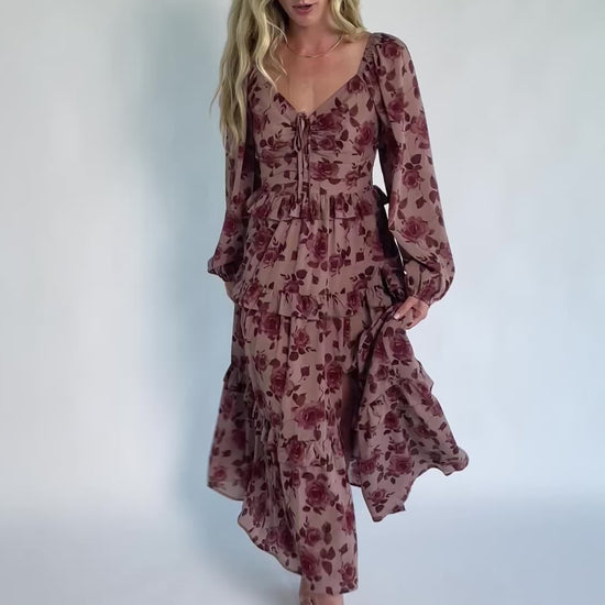 Model wearing a dusty mauve floral maxi dress with a sweetheart neckline, adjustable tie-front bust, and long sheer sleeves.