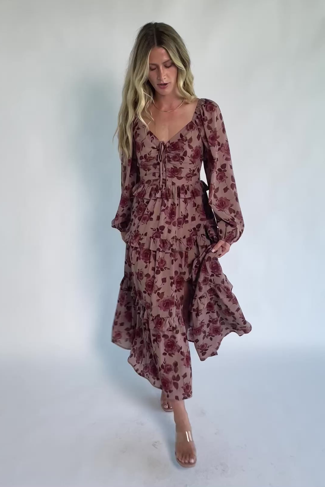Model wearing a dusty mauve floral maxi dress with a sweetheart neckline, adjustable tie-front bust, and long sheer sleeves.