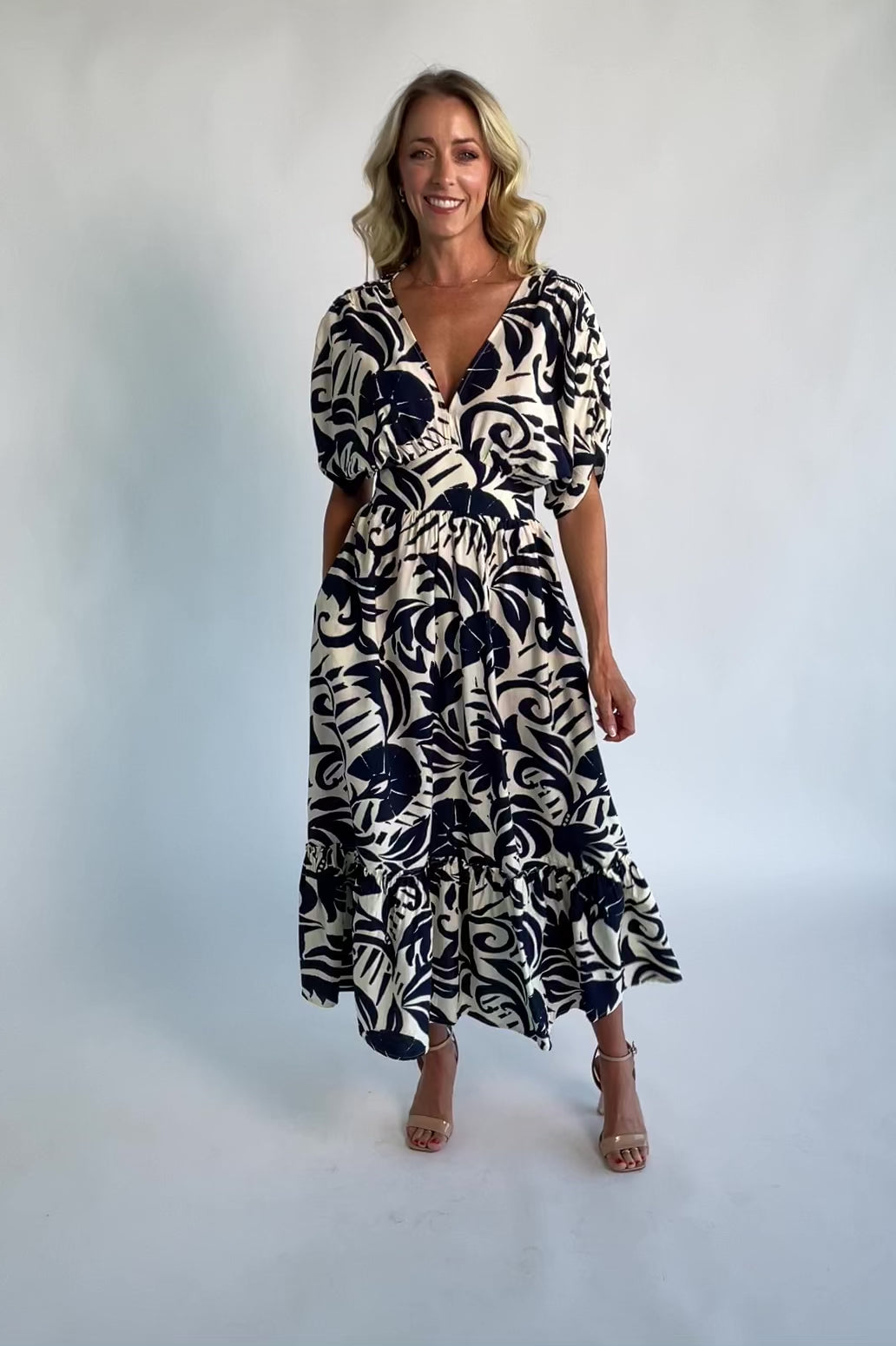 Woman wearing a navy and ivory printed midi dress with a V-neckline, short sleeves, an empire waist, and a tiered hem.