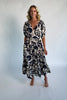 Woman wearing a navy and ivory printed midi dress with a V-neckline, short sleeves, an empire waist, and a tiered hem.