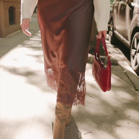 Model wearing the Kamara Satin Lace Skirt in Chocolate featuring a high-rise waistband, bias-cut satin silhouette, delicate floral lace trim at the hem, and a flowing midi length.