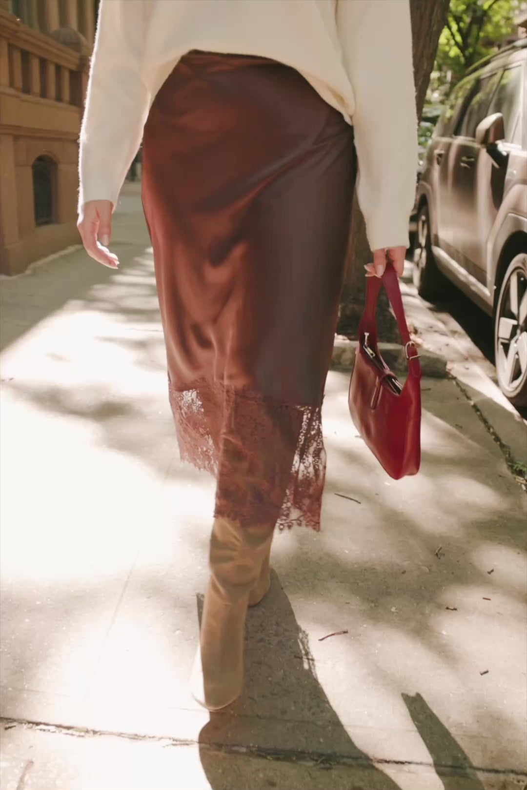 Model wearing the Kamara Satin Lace Skirt in Chocolate featuring a high-rise waistband, bias-cut satin silhouette, delicate floral lace trim at the hem, and a flowing midi length.