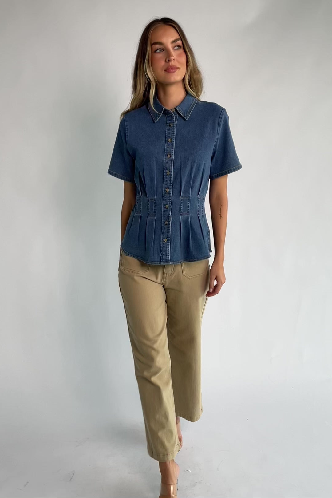 Medium wash stretch denim peplum top with a collared neckline, button-front closure, short sleeves, tailored seam detailing, and a flattering fitted silhouette.