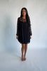 Model wearing a black short lace dress with a sheer floral lace yoke and long sheer sleeves. The dress features a sweetheart-style lined bodice beneath the lace overlay, a round neckline, and a flowy silhouette that falls above the knee.