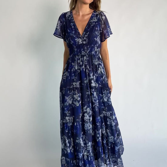 Blue floral chiffon maxi dress with flutter sleeves, surplice V-neck, smocked elastic waist, tiered skirt, and lined body.