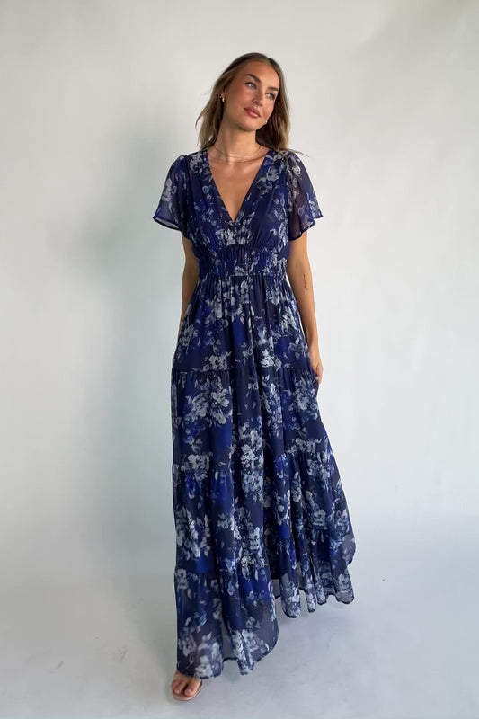 Blue floral chiffon maxi dress with flutter sleeves, surplice V-neck, smocked elastic waist, tiered skirt, and lined body.