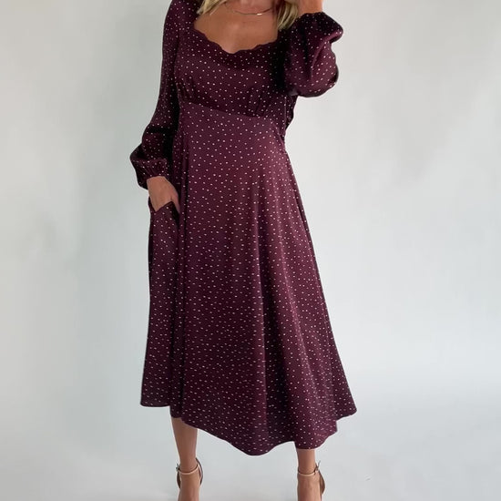 Mahogany brown midi dress with a square neckline, long sleeves, smocked back waist, removable back bow, side pockets, and a flowing skirt with heart details.