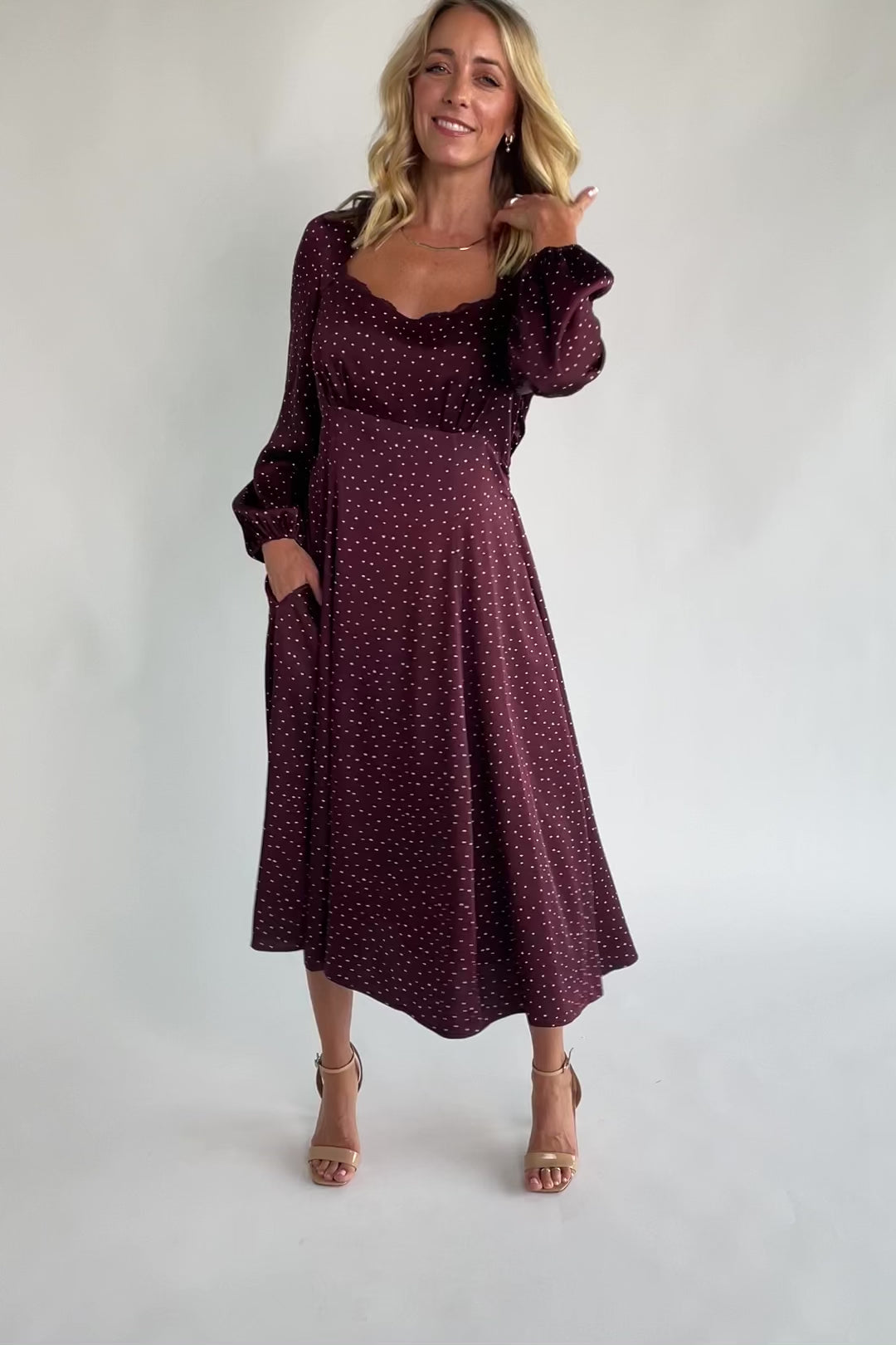 Mahogany brown midi dress with a square neckline, long sleeves, smocked back waist, removable back bow, side pockets, and a flowing skirt with heart details.