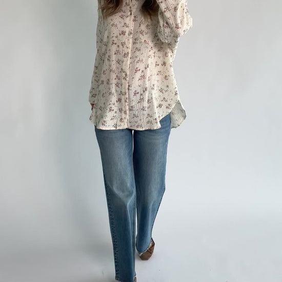 Ivory floral button-front blouse with a collared neckline, long sleeves, front patch pocket, relaxed oversized fit, and rounded high-low hem.