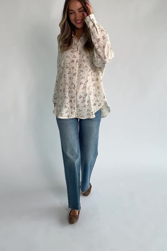 Ivory floral button-front blouse with a collared neckline, long sleeves, front patch pocket, relaxed oversized fit, and rounded high-low hem.