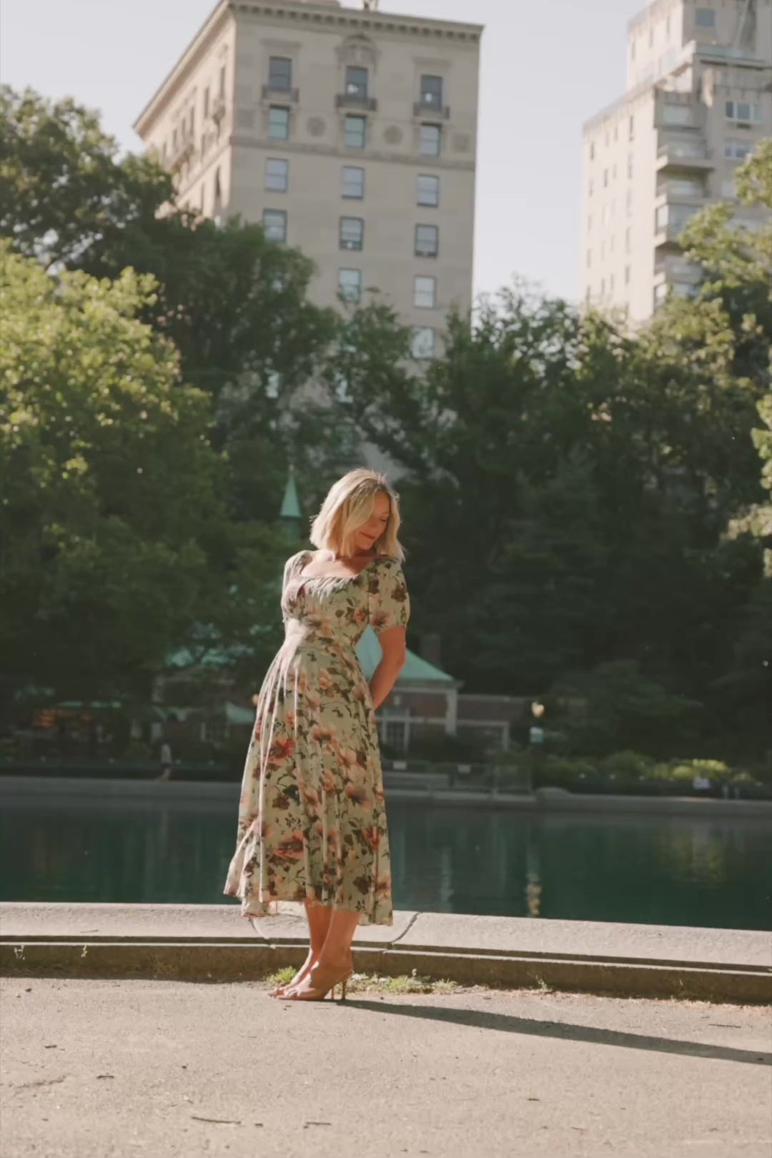 Model wearing the Charlotte Midi Dress in Sage, a sage green midi dress with a pink multi floral print, rounded square neckline, puff sleeves, banded waist, and flowing A-line skirt with side pockets.