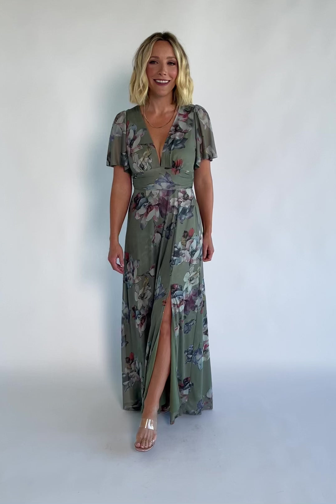 Model wearing a sage floral maxi dress with a deep V-neckline, short flutter sleeves, and an empire waist.
