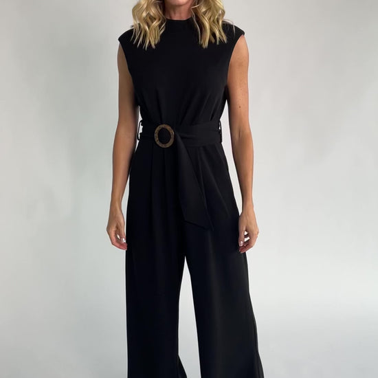 Black tailored wide-leg jumpsuit with a mock neckline, cap sleeves, removable tortoise buckle belt, and side pockets.