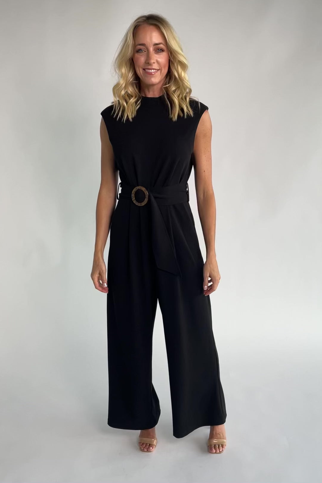 Black tailored wide-leg jumpsuit with a mock neckline, cap sleeves, removable tortoise buckle belt, and side pockets.