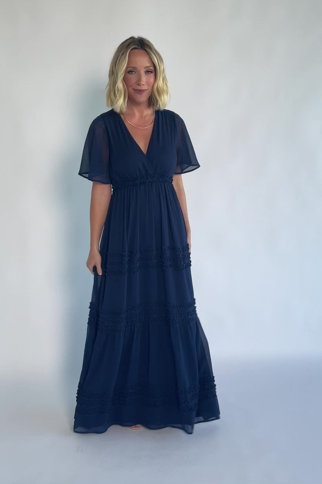 Model wearing a navy chiffon maxi dress with a surplice V-neckline, short ruffled sleeves, and an elastic empire waist.