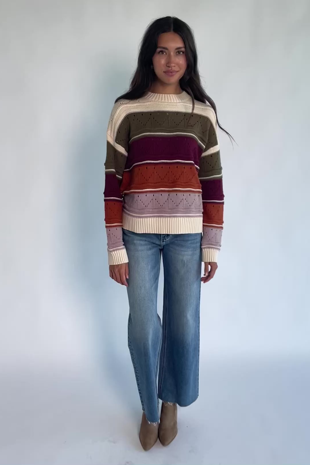 Ivory striped sweater with green, mulberry, rust, and purple horizontal stripes, a round neckline, dropped shoulders, long sleeves, and a relaxed fit.