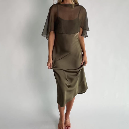 Olive satin midi dress with an attached sheer chiffon cape overlay, round neckline, hidden side zipper, and elegant slip silhouette.