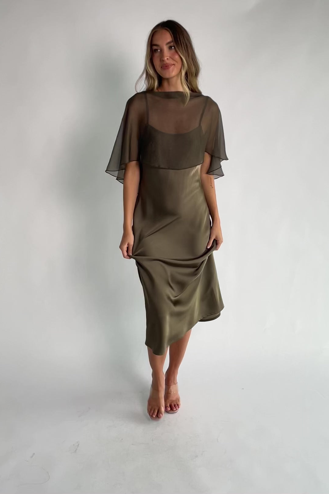 Olive satin midi dress with an attached sheer chiffon cape overlay, round neckline, hidden side zipper, and elegant slip silhouette.