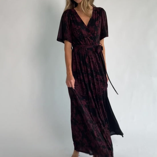 Black and burgundy floral shimmer maxi dress with flutter sleeves, surplice V-neck, elastic waist, removable sash, and side leg slit.