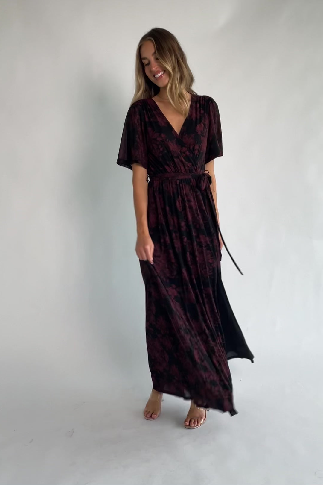 Black and burgundy floral shimmer maxi dress with flutter sleeves, surplice V-neck, elastic waist, removable sash, and side leg slit.