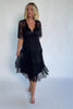Model wearing a black lace midi dress with a deep V-neckline, short sheer scalloped sleeves, and an elastic waist.