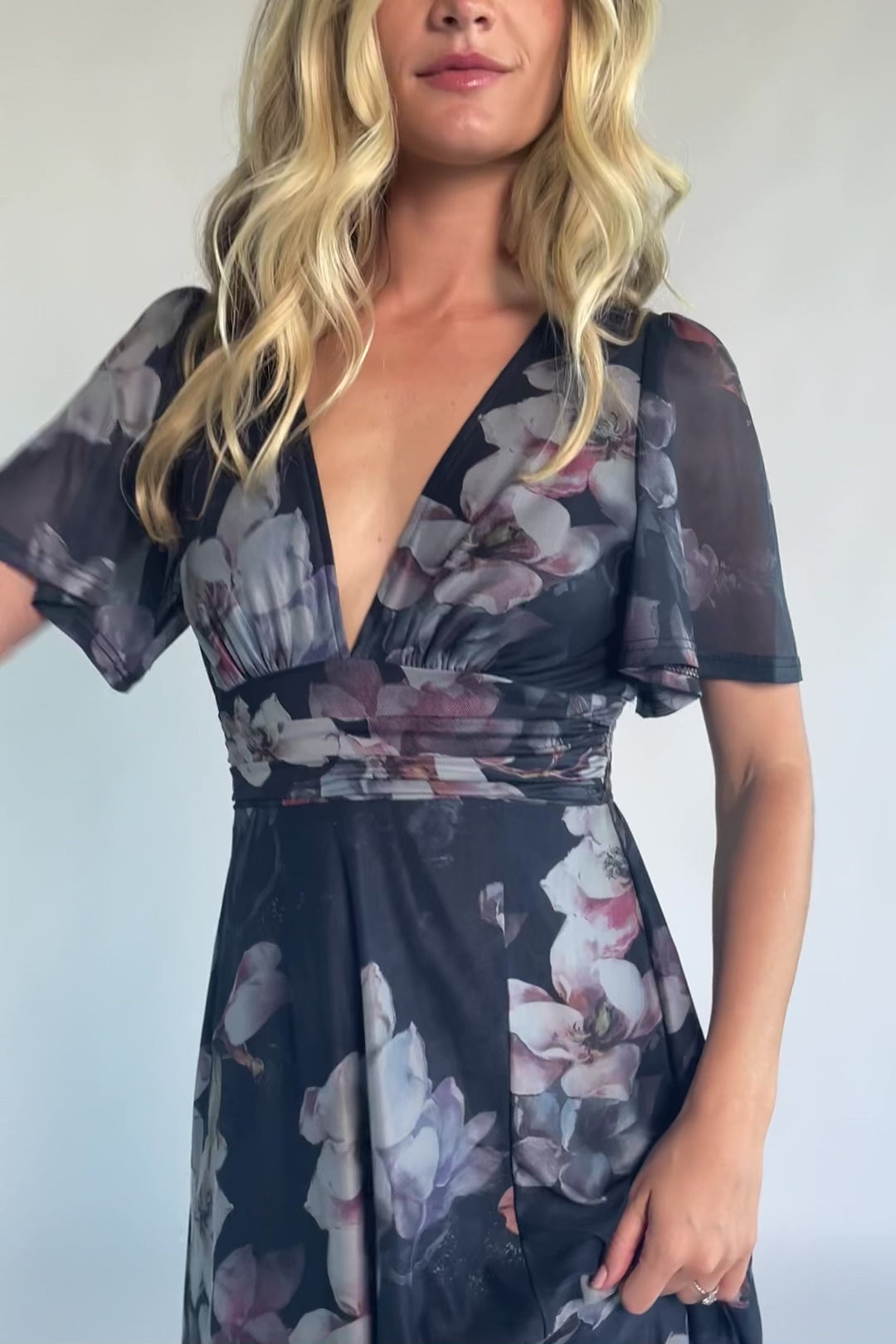 Model wearing a deep blue floral maxi dress with a deep V-neckline, short flutter sleeves, and an empire waist.