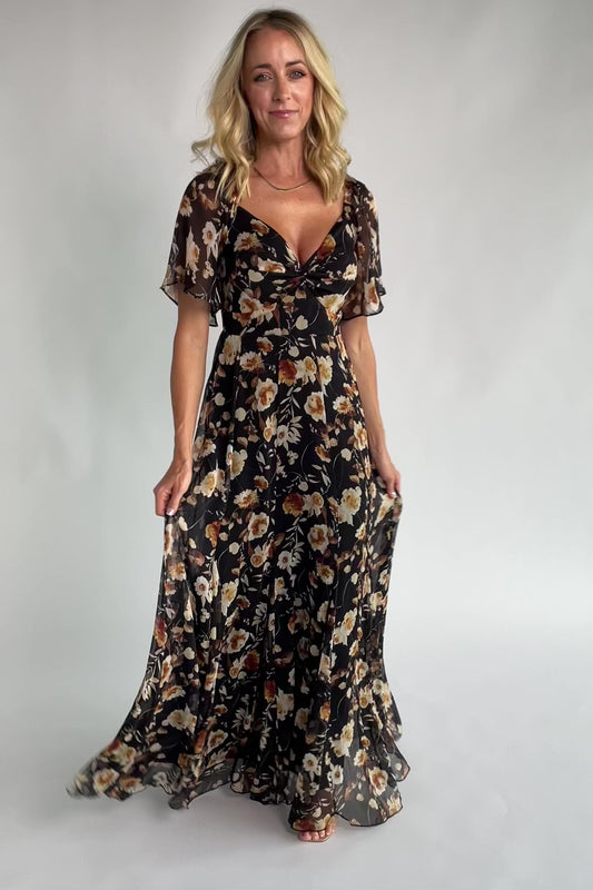 Black floral chiffon maxi dress with a sweetheart neckline, flutter sleeves, smocked back bodice, tiered skirt, and subtle gold foil detailing.
