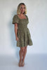Model wearing an olive floral short dress with a square neckline, fully smocked bodice, and short balloon sleeves.