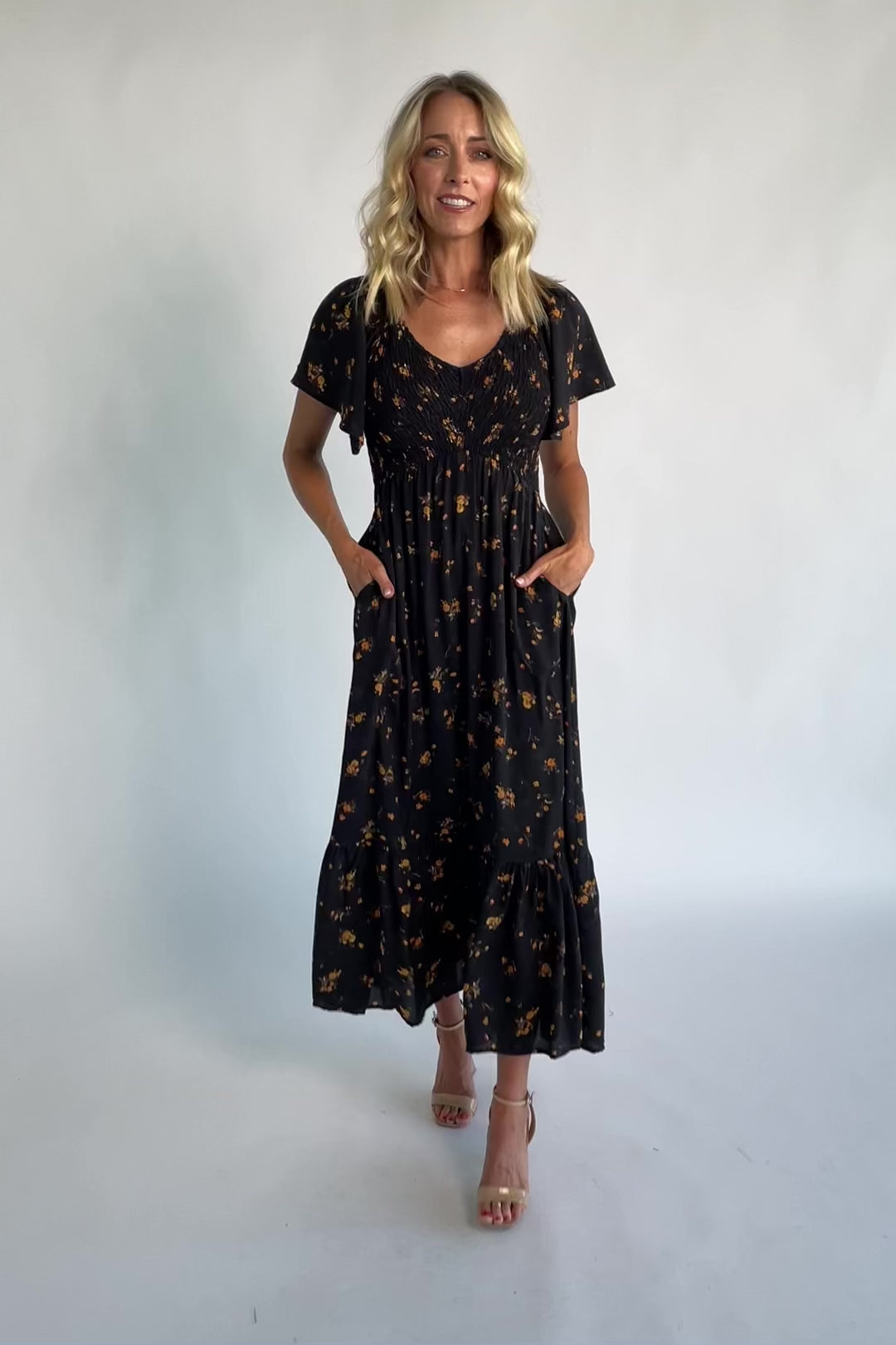 Model wearing a floral midi dress with a smocked bodice, wide V-neckline, and flutter sleeves.