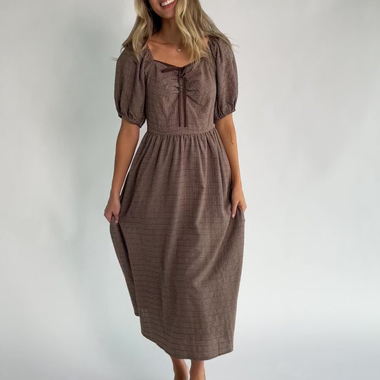 Mocha gingham midi dress with a square neckline, puff sleeves, smocked back, side pockets, and a flowing tiered skirt.
