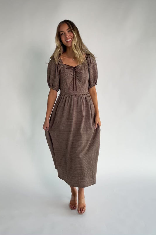 Mocha gingham midi dress with a square neckline, puff sleeves, smocked back, side pockets, and a flowing tiered skirt.