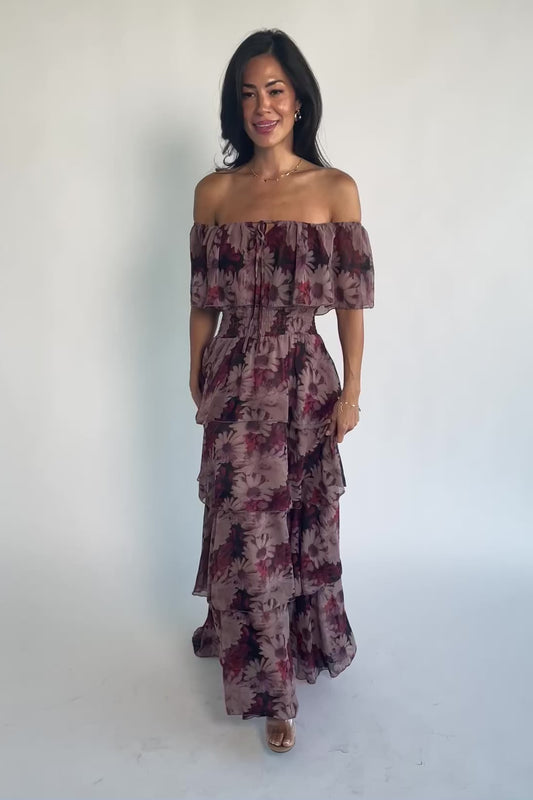Model wearing the Carina Off-Shoulder Maxi in a soft multi floral print featuring a versatile neckline that can be worn on or off the shoulders, a ruffle overlay across the bust, a smocked waist, and a flowing four-tier maxi skirt.