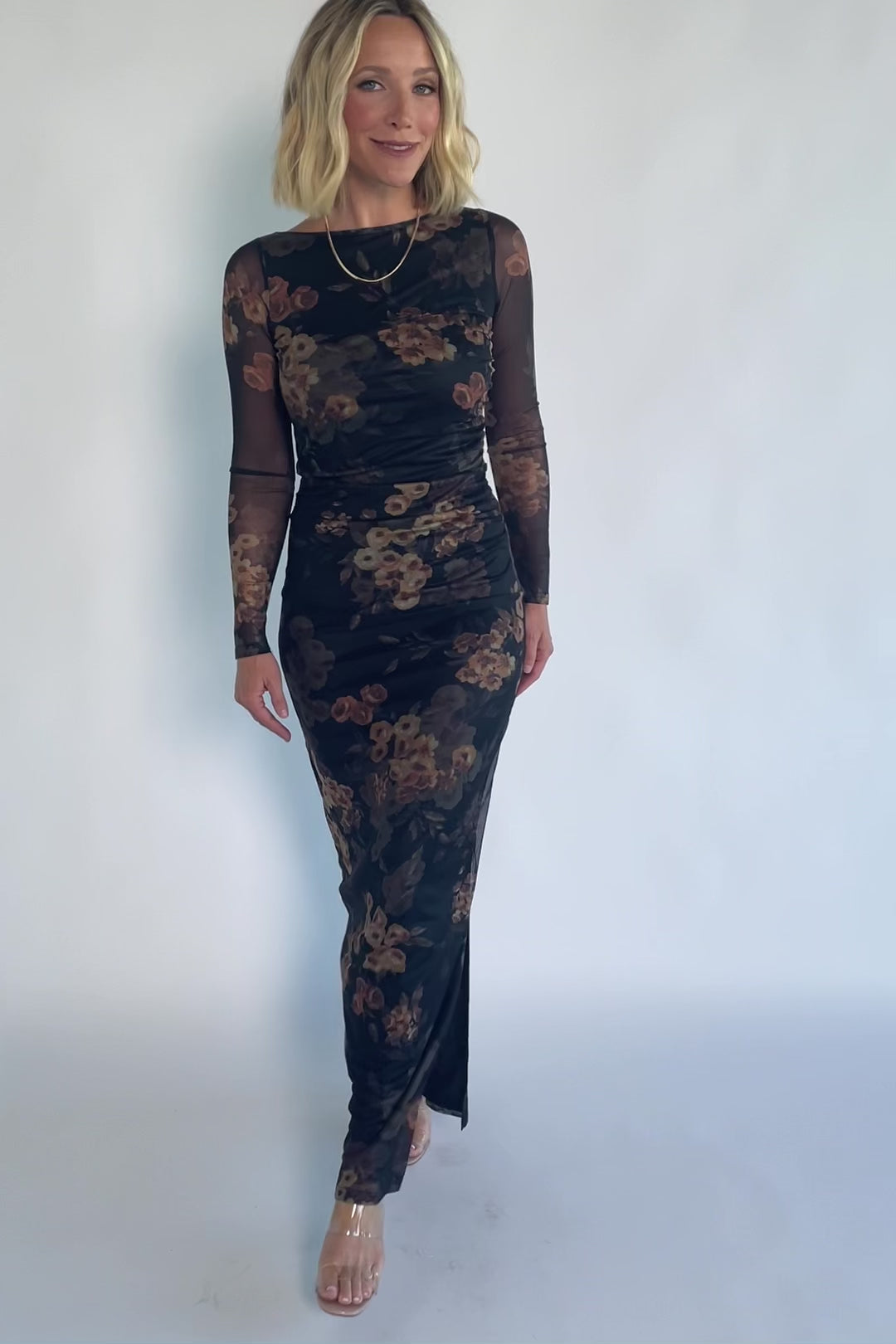 Black mesh bodycon midi dress with muted gold floral print, sheer long sleeves, a round neckline, flattering side ruching, and a thigh-high side slit.